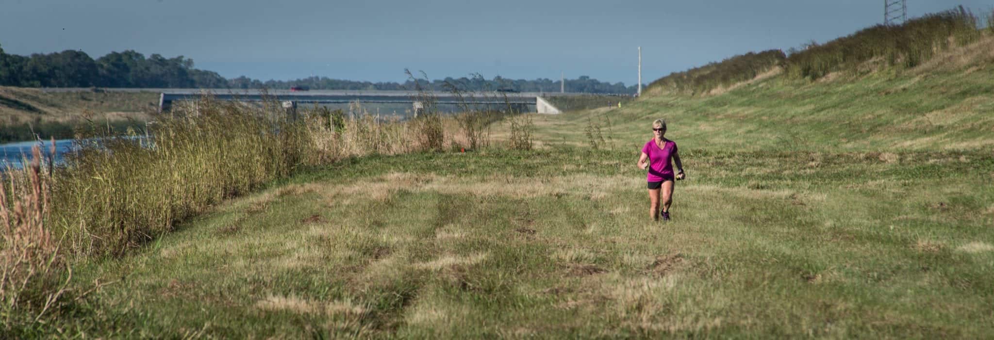 Image of a female ultra marathon participant running over a meadow next to a river