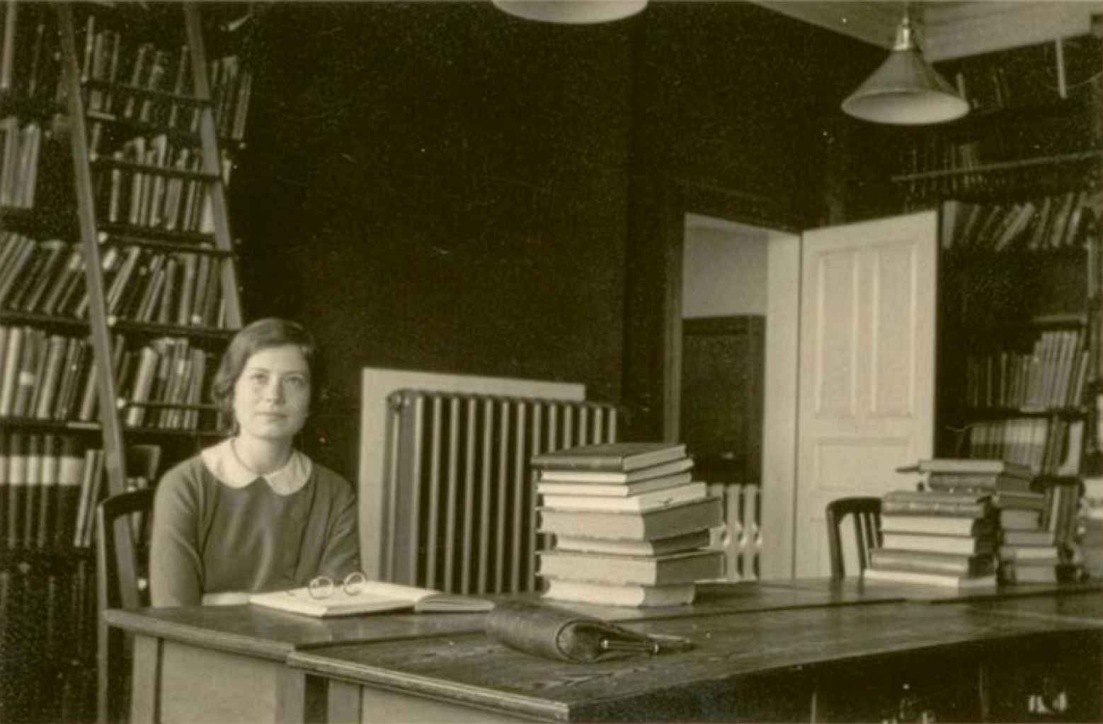 Black and white photograph of Hedwig Klein sitting in front of an open folder in a library